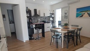 Une cuisine moderne dotée d’un îlot central, un coin repas avec une table ronde et des chaises, et un canapé blanc dans l’espace de vie.