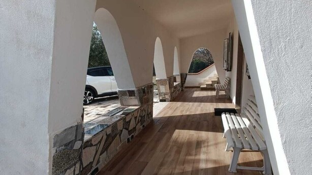 Un espace extérieur abrité, doté d’un sol en pierre et en bois, de murs blancs et d’un banc.