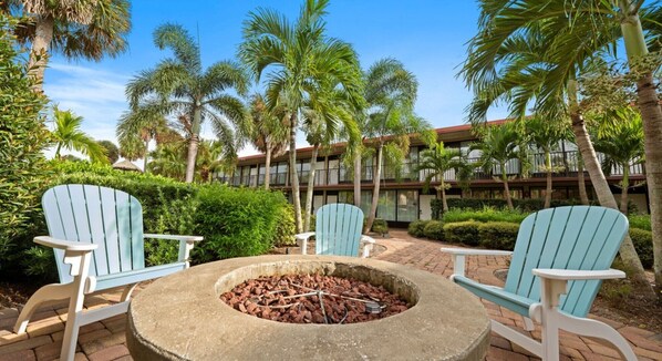 An outdoor seating area with Adirondack chairs and a stone fire pit surrounded by lush greenery and palm trees. - Big Fun, Small Price—Your Orlando Escape! (Kissimmee)