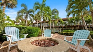 An outdoor seating area with Adirondack chairs and a stone fire pit surrounded by lush greenery and palm trees. - Close to Disney, Far from Pricey! (Kissimmee)