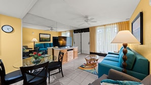 A well-lit living room with a blue sofa, a dining table with chairs, a TV, and a ceiling fan. - Close to Disney, Far from Pricey! (Kissimmee)