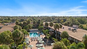 An aerial view of a resort with a swimming pool, lounge areas, and palm trees. - Park-Hopping Made Easy | 2BR Retreat Near Disney & Universal (Kissimmee)