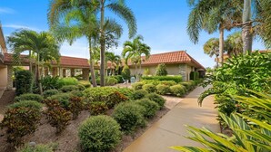 A courtyard with palm trees, a pathway, and a building with a red-tiled roof. - Park-Hopping Made Easy | 2BR Retreat Near Disney & Universal (Kissimmee)