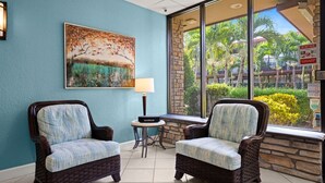 A room with two wicker chairs, a painting, a lamp, and a view of a garden through large windows. - Park-Hopping Made Easy | 2BR Retreat Near Disney & Universal (Kissimmee)