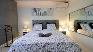A neatly made bed with a floral bedspread, two bedside lamps, a headboard with a mirror, and a wall-mounted air conditioner. - Magnificent villa with heated pool near La Citée (Carcassonne)