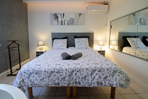 A neatly made bed with a floral bedspread, two bedside lamps, a headboard with a mirror, and a wall-mounted air conditioner.