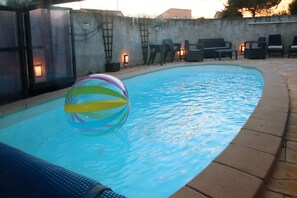 A swimming pool with a colorful ball, surrounded by chairs and a wall with a ladder.