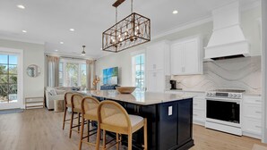 Una cucina moderna con un'isola grande, mobili bianchi, forno integrato e lampadario a sospensione.