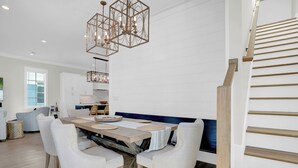 Zona pranzo moderna con tavolo in legno, sedie imbottite bianche e lampadario geometrico.