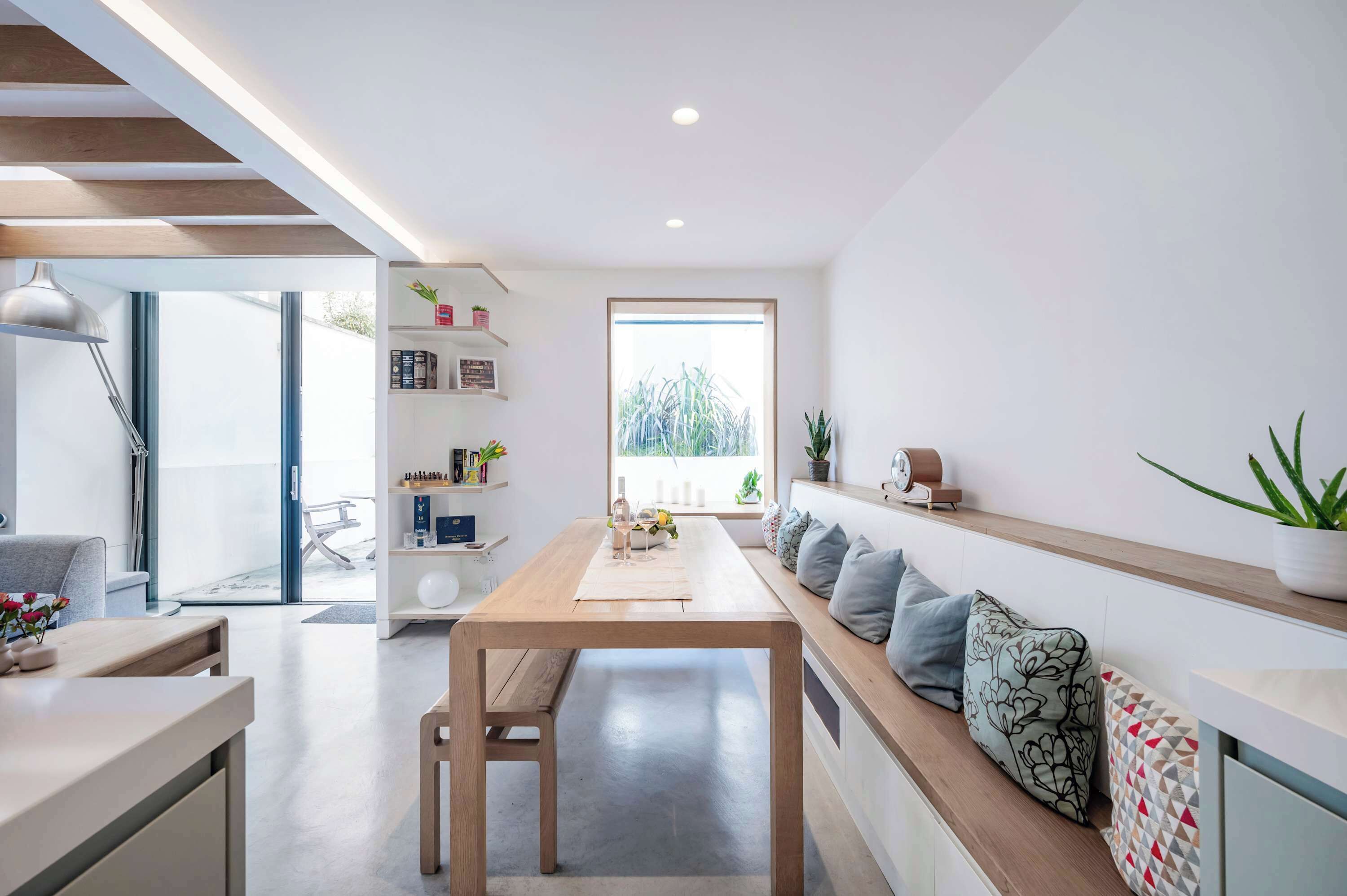 A modern interior with a wooden dining table, bench seating, and a bookshelf.