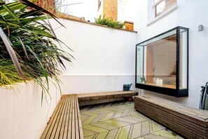Un espacio exterior moderno con un banco de madera, una pared de vidrio y un suelo de baldosas tipo espiga.