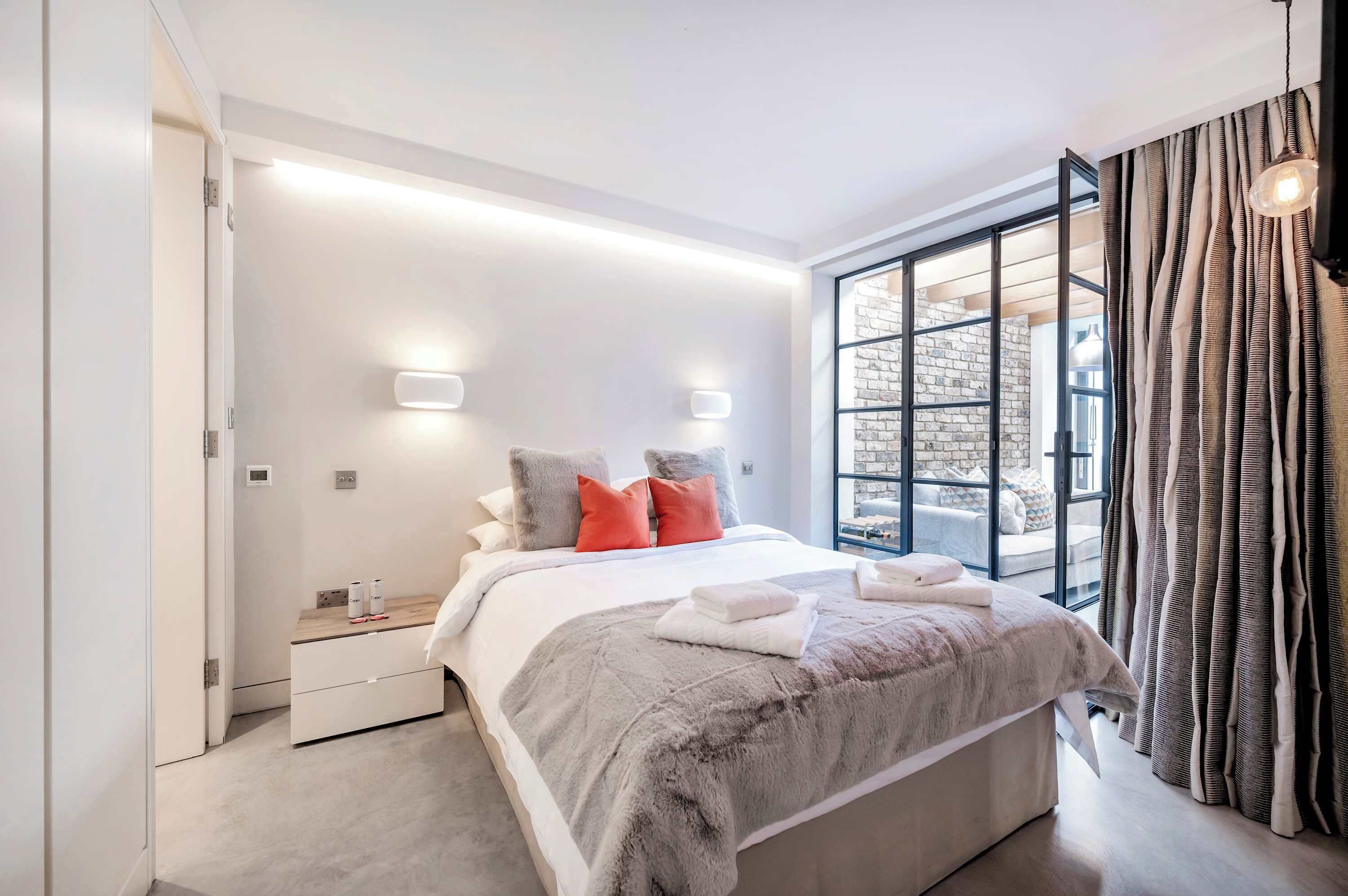 A modern bedroom with a large bed, bedside tables, a view through a glass door, and a curtain.