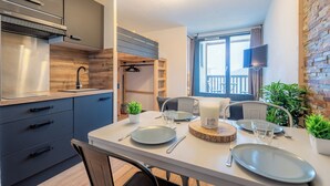 A modern kitchen with grey cabinets, a stainless steel range hood, and a wooden backsplash. There is a dining area with a white table set for two, including plates, cutlery, and a candle. - Cimes des caron  (Les Belleville)