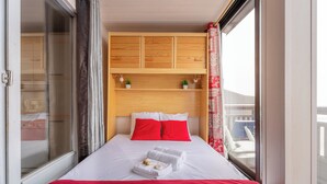 A hotel room with a bed, a wooden headboard, a window with a view, and a red curtain. - Cimes des caron  (Les Belleville)