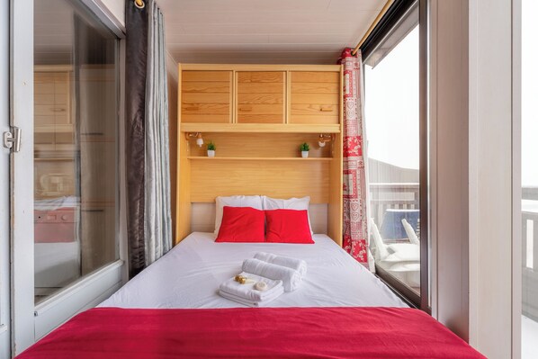 Une chambre d’hôtel avec un lit, une tête de lit en bois, une fenêtre donnant sur un paysage agréable et un rideau rouge.