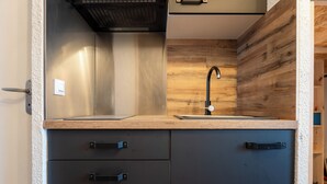 A kitchen with a wooden backsplash, a black faucet, and two black cabinets with handles. - Cimes des caron  (Les Belleville)