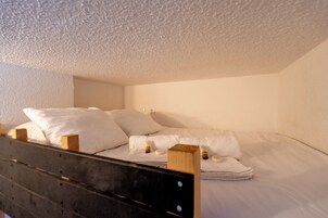Un lit simple avec une literie et des oreillers blancs, une tête de lit en bois et un petit tabouret en bois.