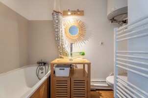 A bathroom with a bathtub, a sink with a glass bowl, a wooden vanity, a shower, and a toilet.