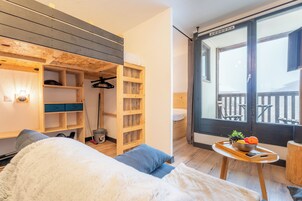 Una stanza accogliente con un letto, un mobiletto a mensole in legno, un tavolino con un vassoio di frutta e un balcone con vista.