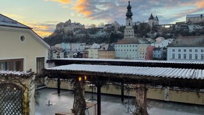 A courtyard with a pergola, steps leading to a building, and a view of a historic town with a castle-like structure in the background. - Gästehaus Burgblick im Weinhaus Pachler (Hochburg-Ach)