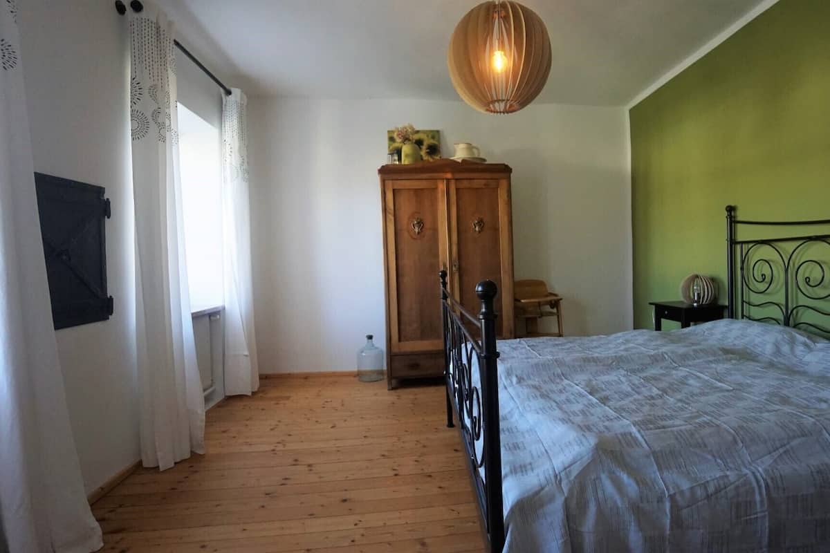 Ein Schlafzimmer mit Holzboden, einem Bett mit Metallgestell, einem Holzschrank und einer grünen Wand.