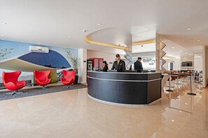 A modern hotel lobby with a reception desk, red chairs, and a large wall mural. - Edifício João Bettega (Curitiba)