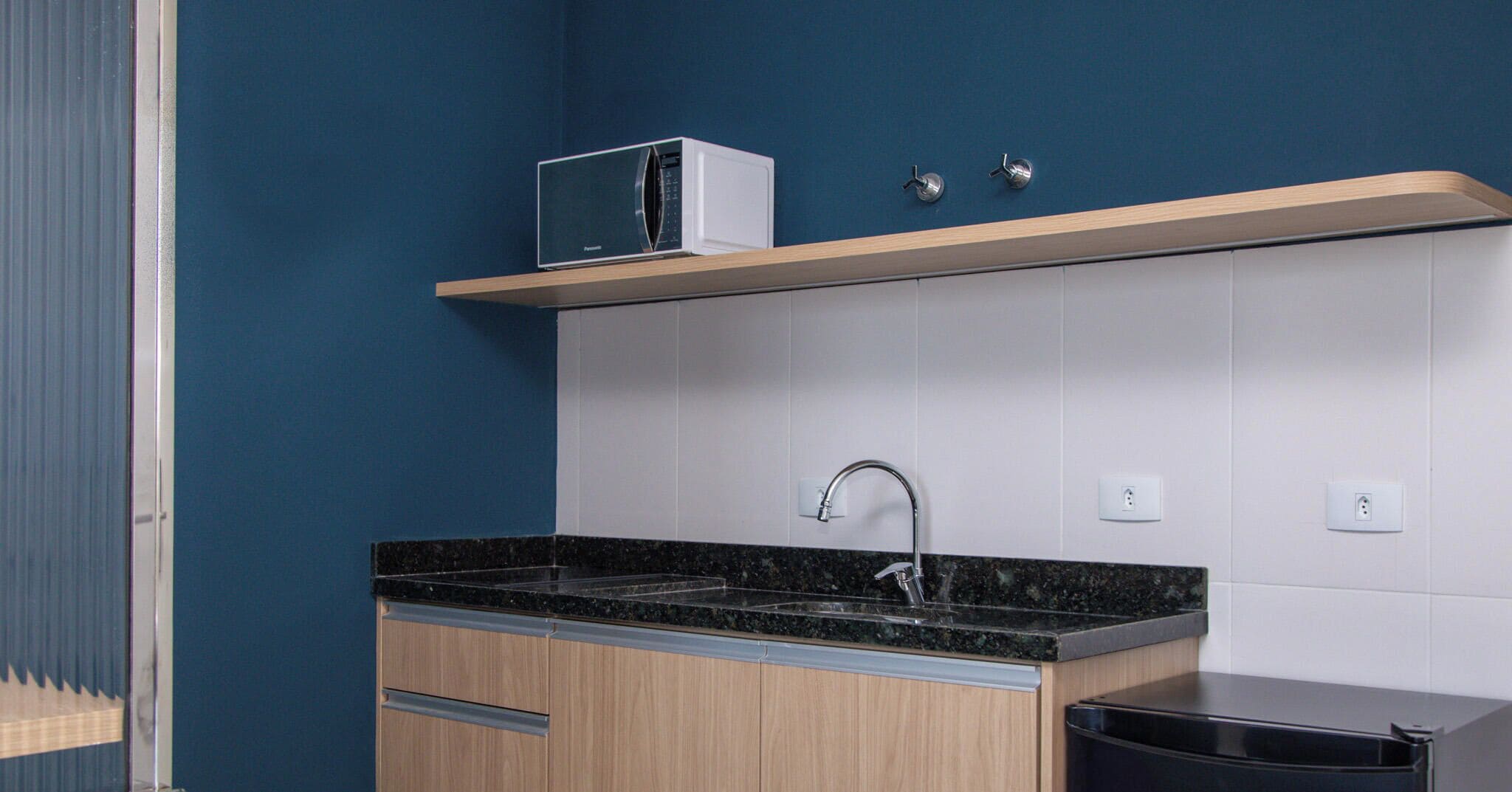 A modern kitchen with a black countertop, wooden cabinets, a microwave, and a black trash bin.