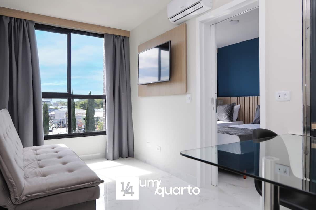 A modern hotel room with a large window, a sofa, a bed, and a glass table.
