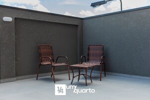 Terraço no telhado com duas cadeiras de vime e um candeeiro.