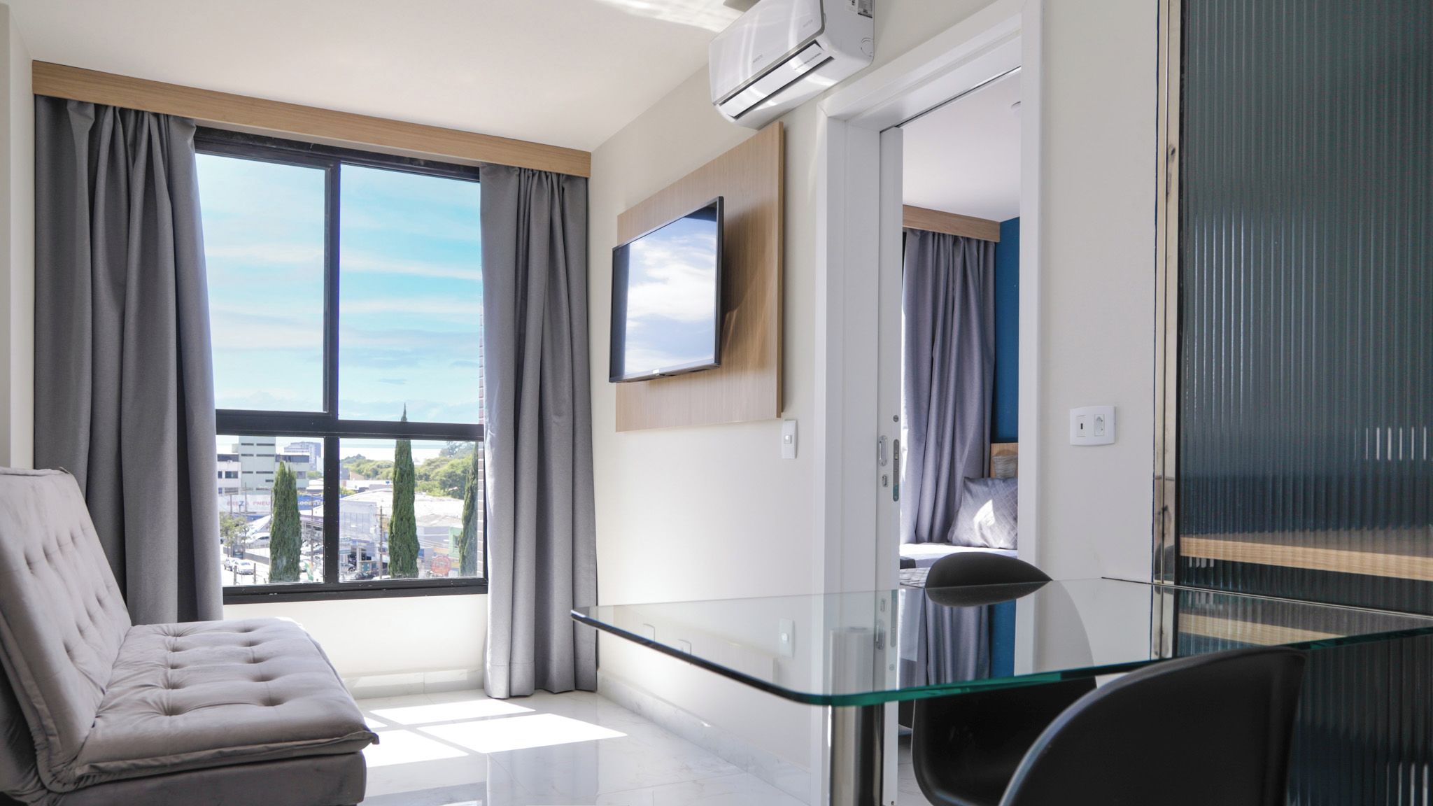 Uma sala de estar moderna com uma mesa de centro de vidro, um sofá e uma TV fixada na parede.