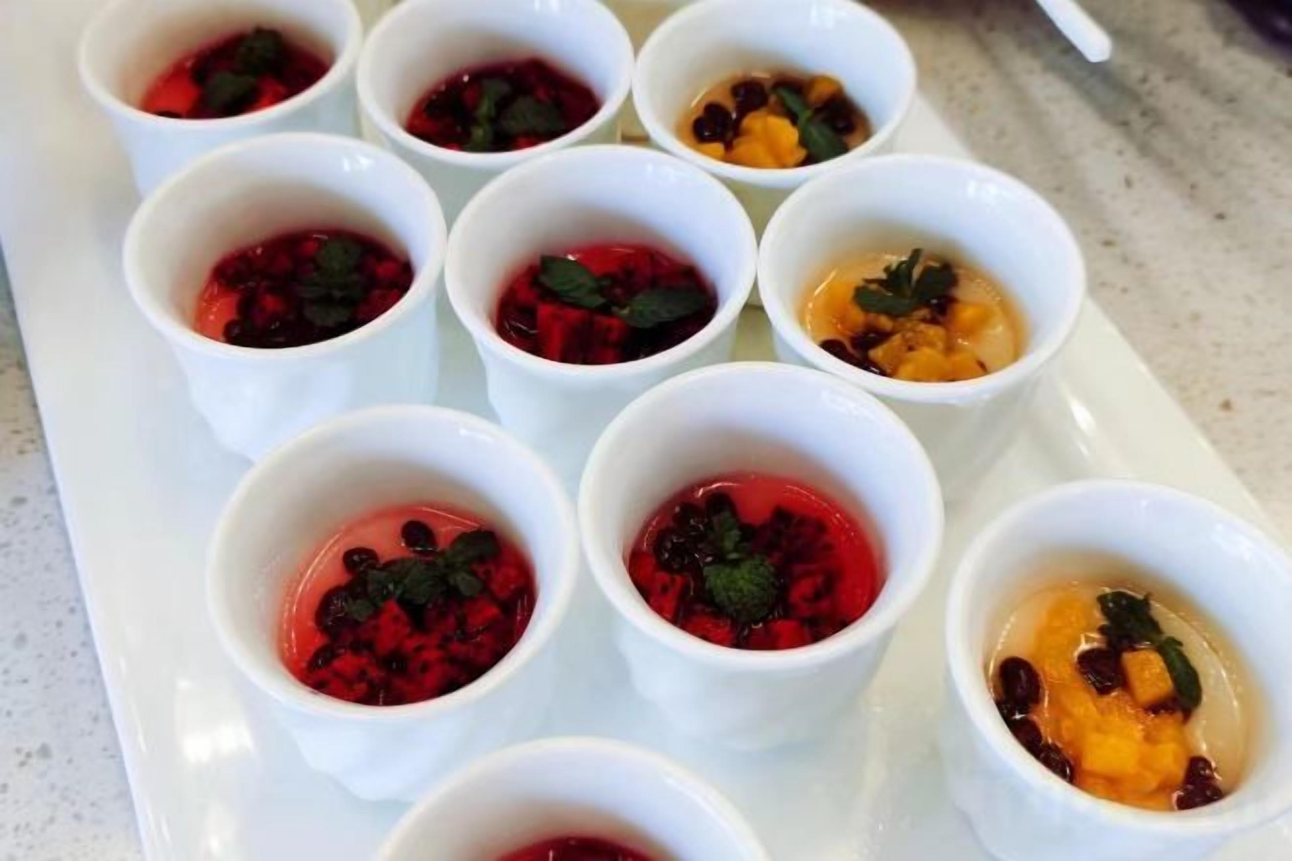 A tray of small white cups with various food items, possibly desserts, arranged on a white plate.