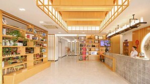 Um hall amplo com prateleiras de madeira repletas de livros e plantas, um balcão de recepção e piso de azulejos.