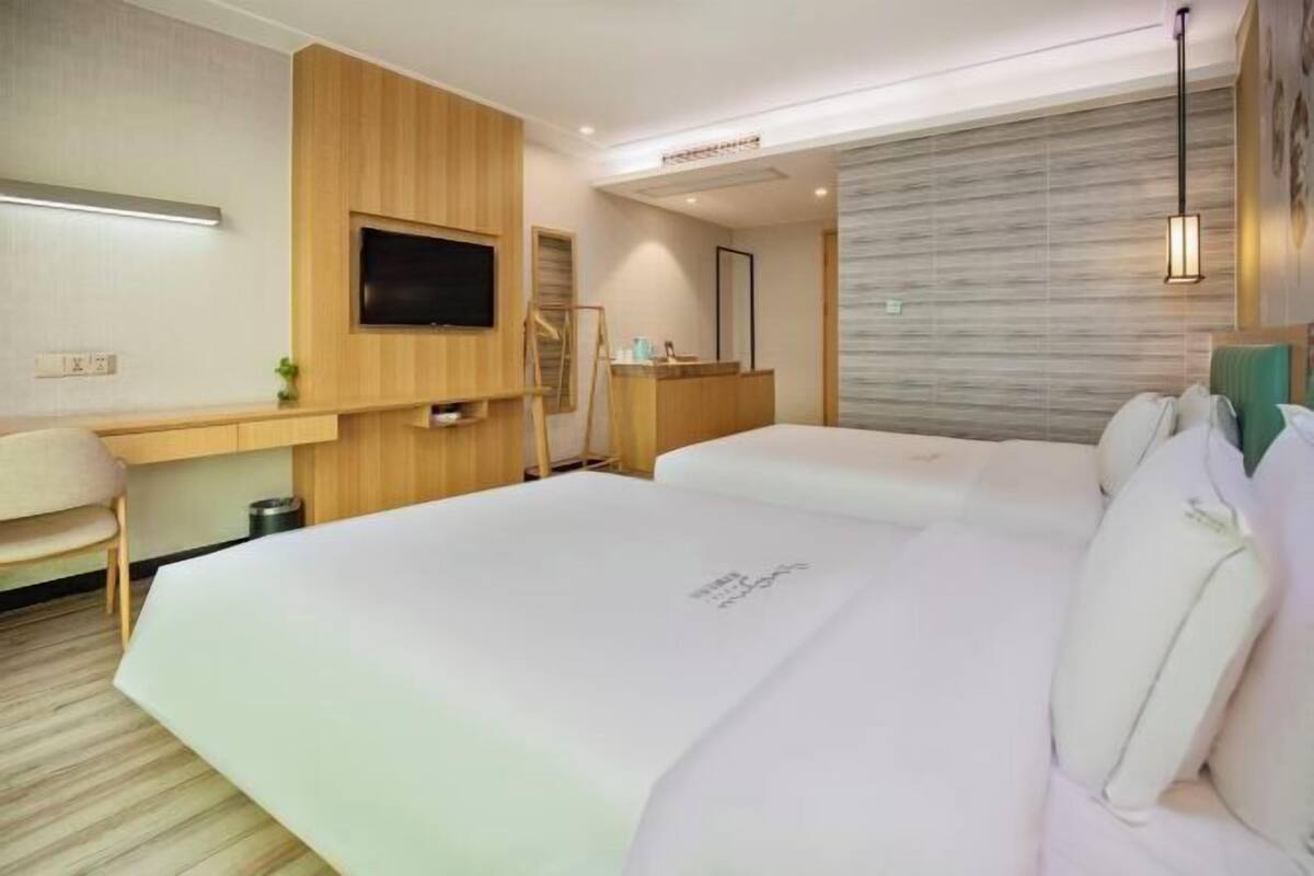 Ein Hotelzimmer mit zwei Betten, einem Schreibtisch, einem Fernseher und einem Spiegel.