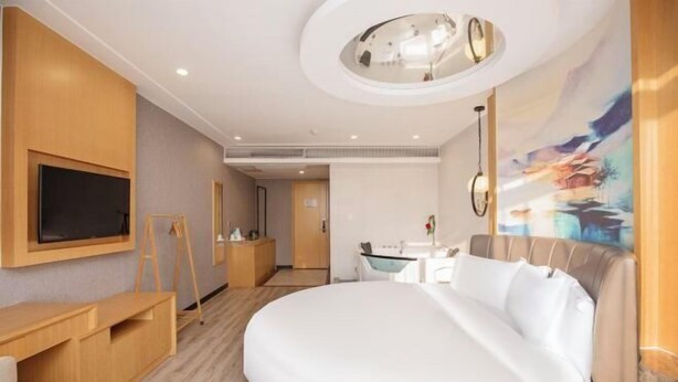 Quarto de hotel moderno com uma cama grande, uma escrivaninha, uma televisão na parede e um quadro na parede.