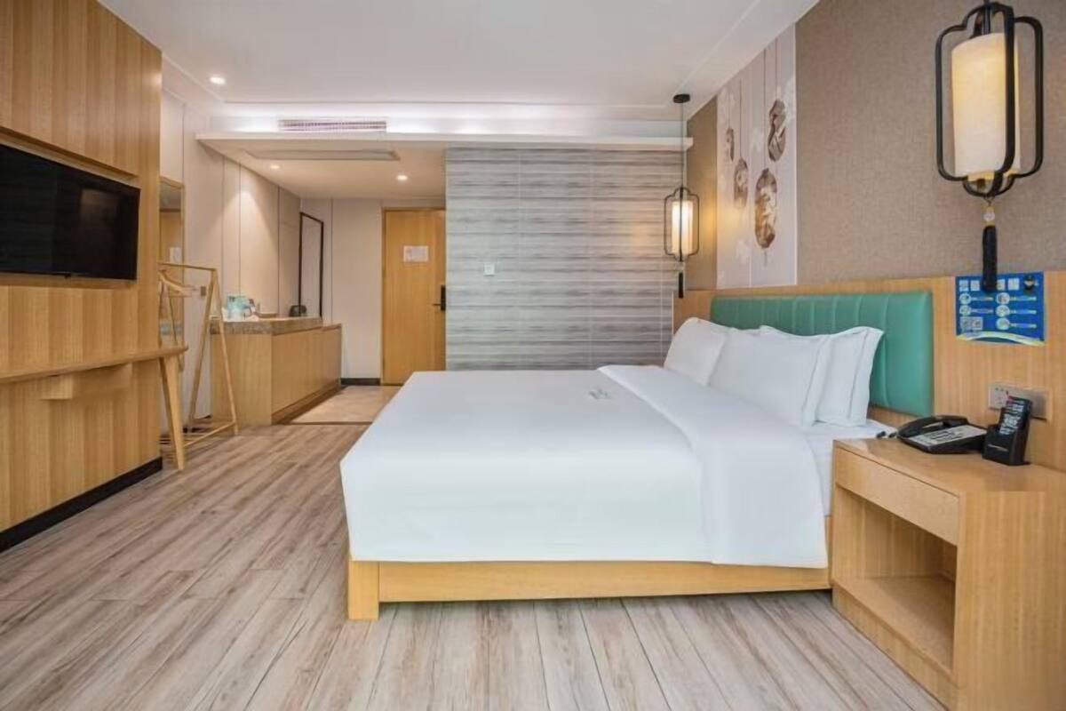 Ein Hotelzimmer mit einem Bett, Holzmöbeln, einem Fernseher und einer Wandleuchte.
