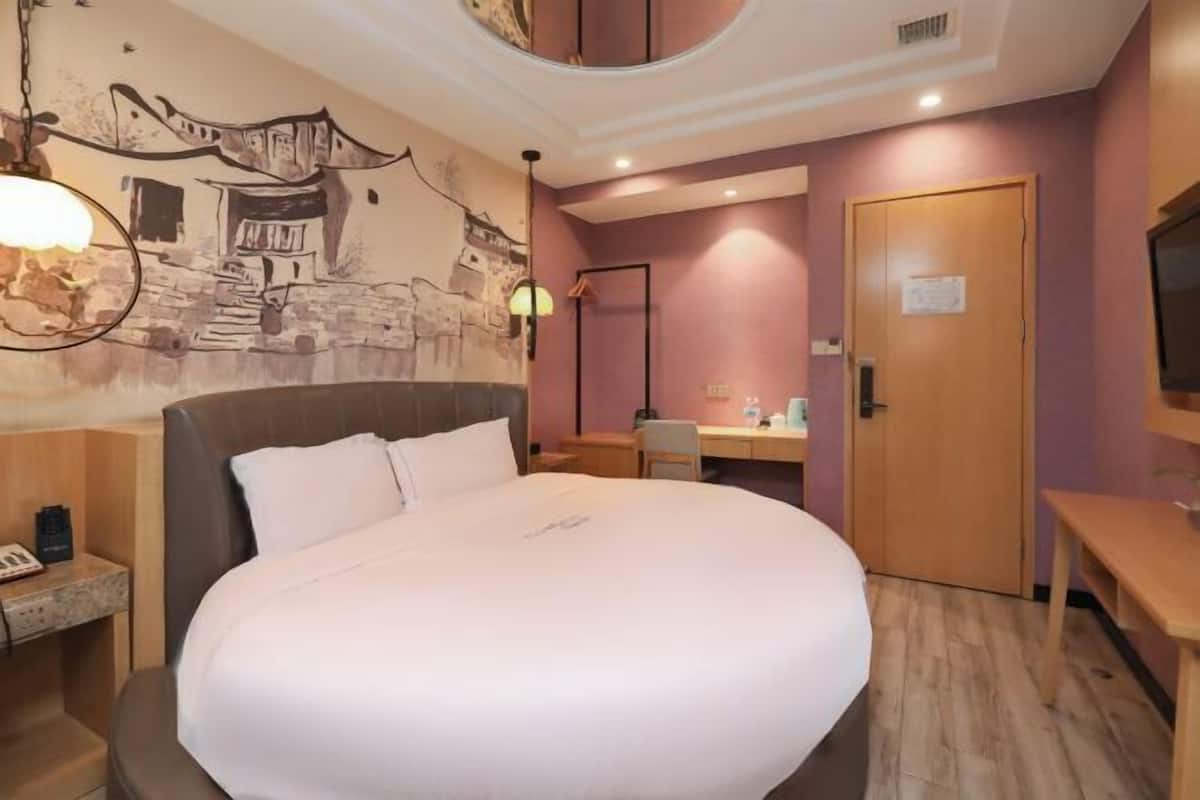 Ein Hotelzimmer mit einem großen Bett, einem Schreibtisch, einem Stuhl, einem Spiegel und einer Wand mit Wandgemälde.
