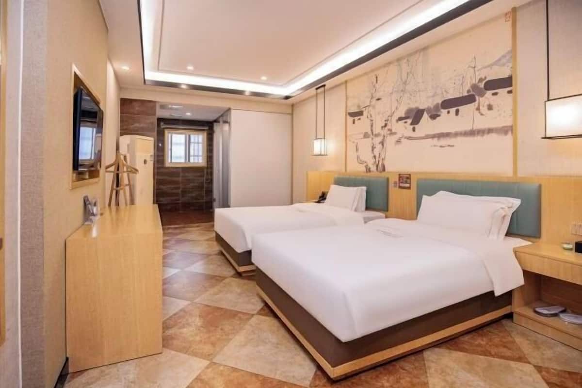 Ein Hotelzimmer mit zwei Betten, einem Holztisch, einem Flachbildfernseher und einem großen Wandbild.