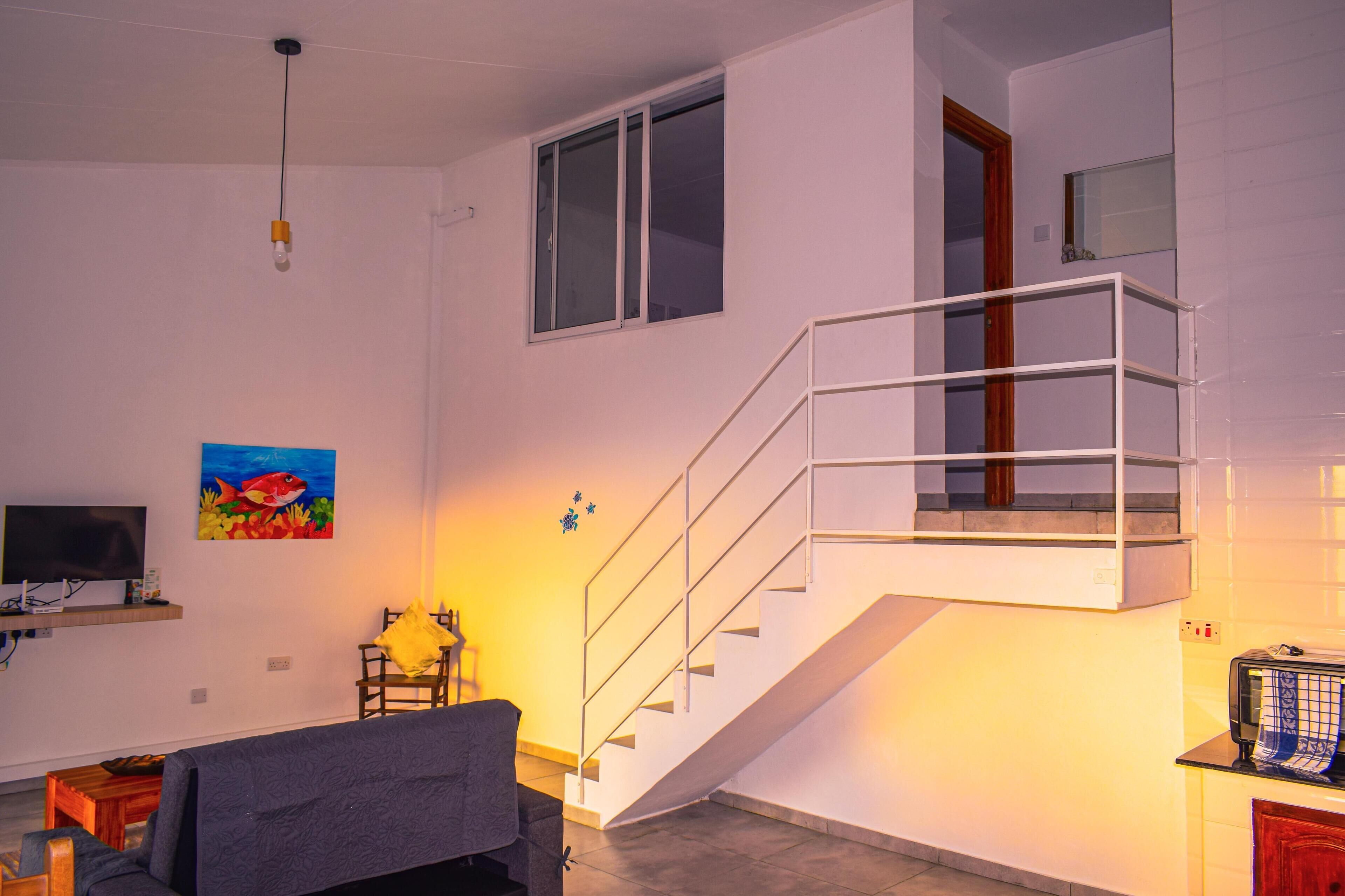 Un salon moderne avec un escalier, un téléviseur à écran plat, un tableau et un coin repas.