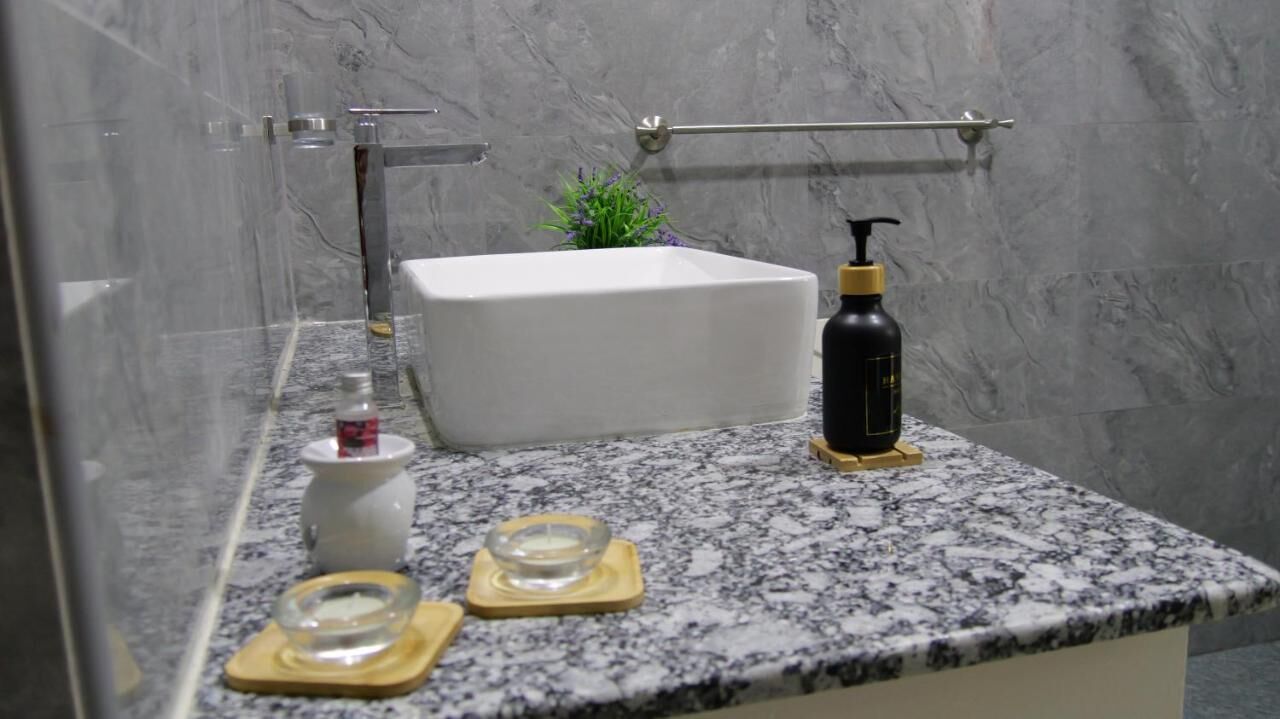 A bathroom with a white bathtub, a marble countertop, a soap dispenser, and a small plant.