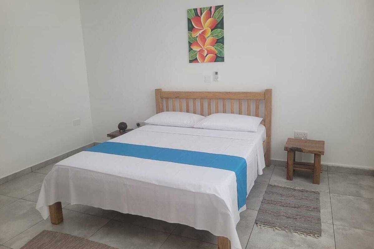 A single bed with a wooden headboard, white bedding, and a blue accent. There is a small wooden nightstand beside the bed.