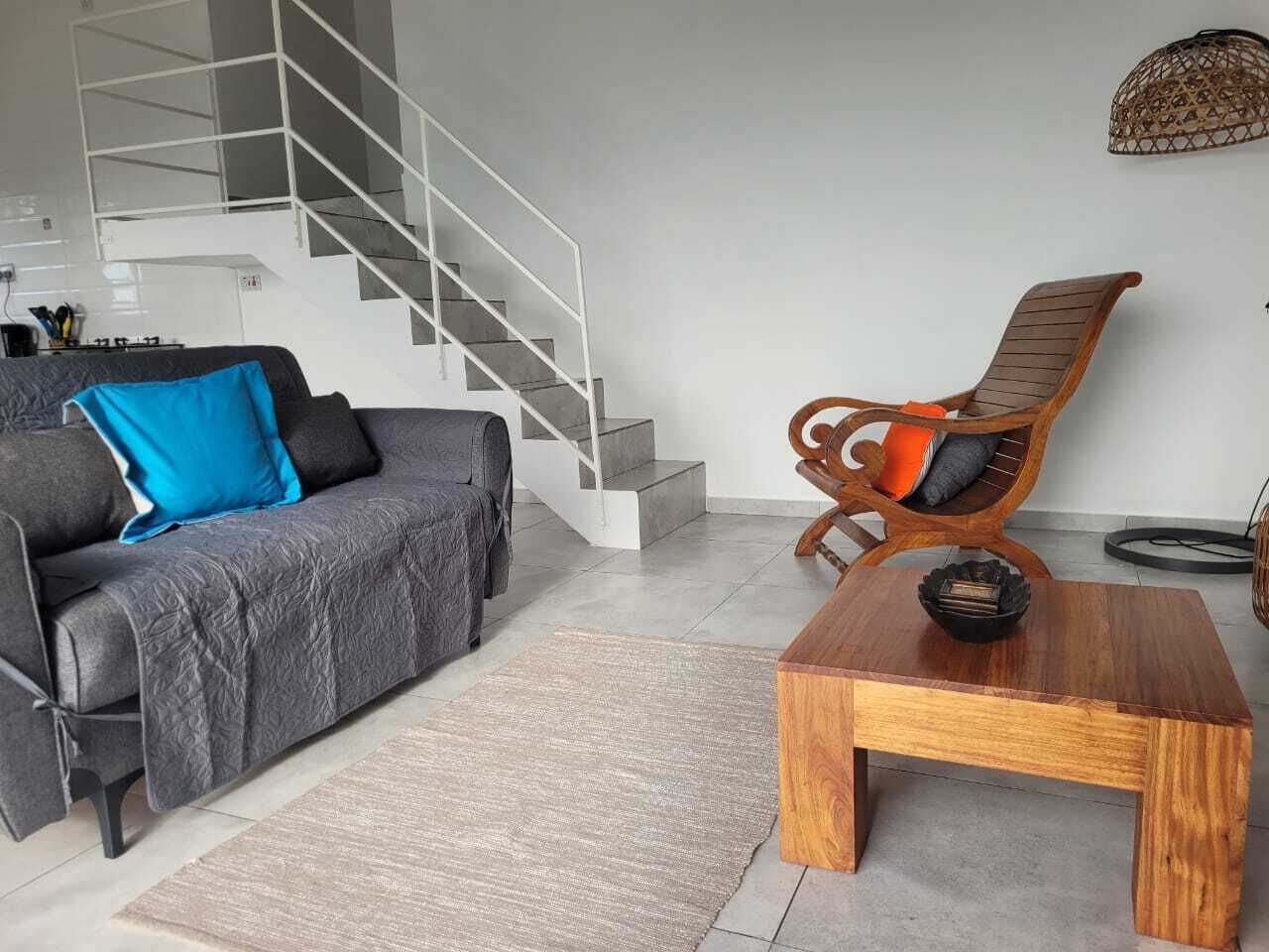 Una sala de estar moderna con un sofá gris, una mesa de centro de madera y una silla de mimbre.