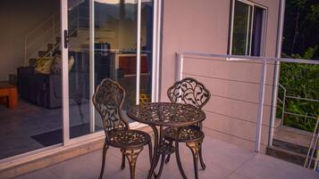 A patio with a glass door leading to a staircase, a round metal table with chairs, and a view of a building with a window and a door.