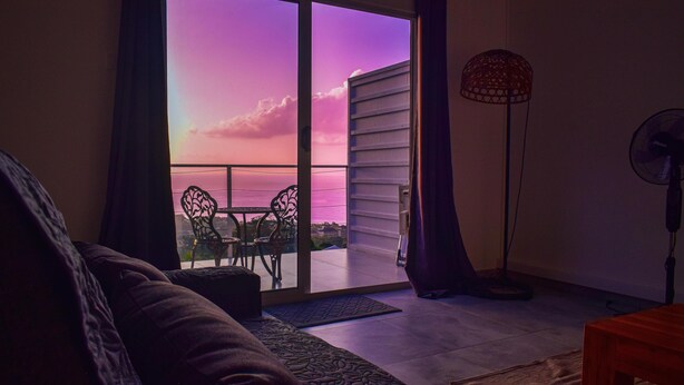 Ein Zimmer mit einer großen Schiebeglastür, die auf einen Balkon führt, einem Standventilator und einem Sofa.