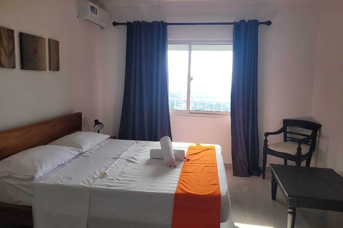 A hotel room with a bed, a chair, a table, and a window with curtains.