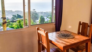 Ein Essbereich mit Holztisch und Stühlen, Blick auf das Meer und einem Fenster mit Vorhang.