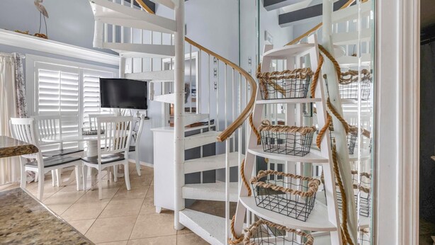 A spacious living area with a white staircase, a flat-screen TV, and a dining set. - GS Plantation West 1339 (Gulf Shores)