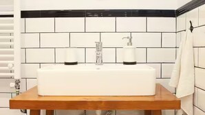 Un baño con lavamanos blanco, salpicadero con azulejos blanco y negro, y un espejo redondo con diseños geométricos.