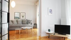 Una sala de estar moderna con un sofá gris, dos cuadros enmarcados, una mesa de centro redonda, un televisor sobre un mueble bajo y suelo de madera.