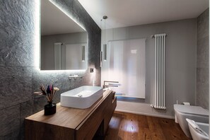 Ein modernes Badezimmer mit einem großen Spiegel, einem rechteckigen Waschbecken, einer Holz-Kommode, einer Dusche mit Glastür und einer Toilette.