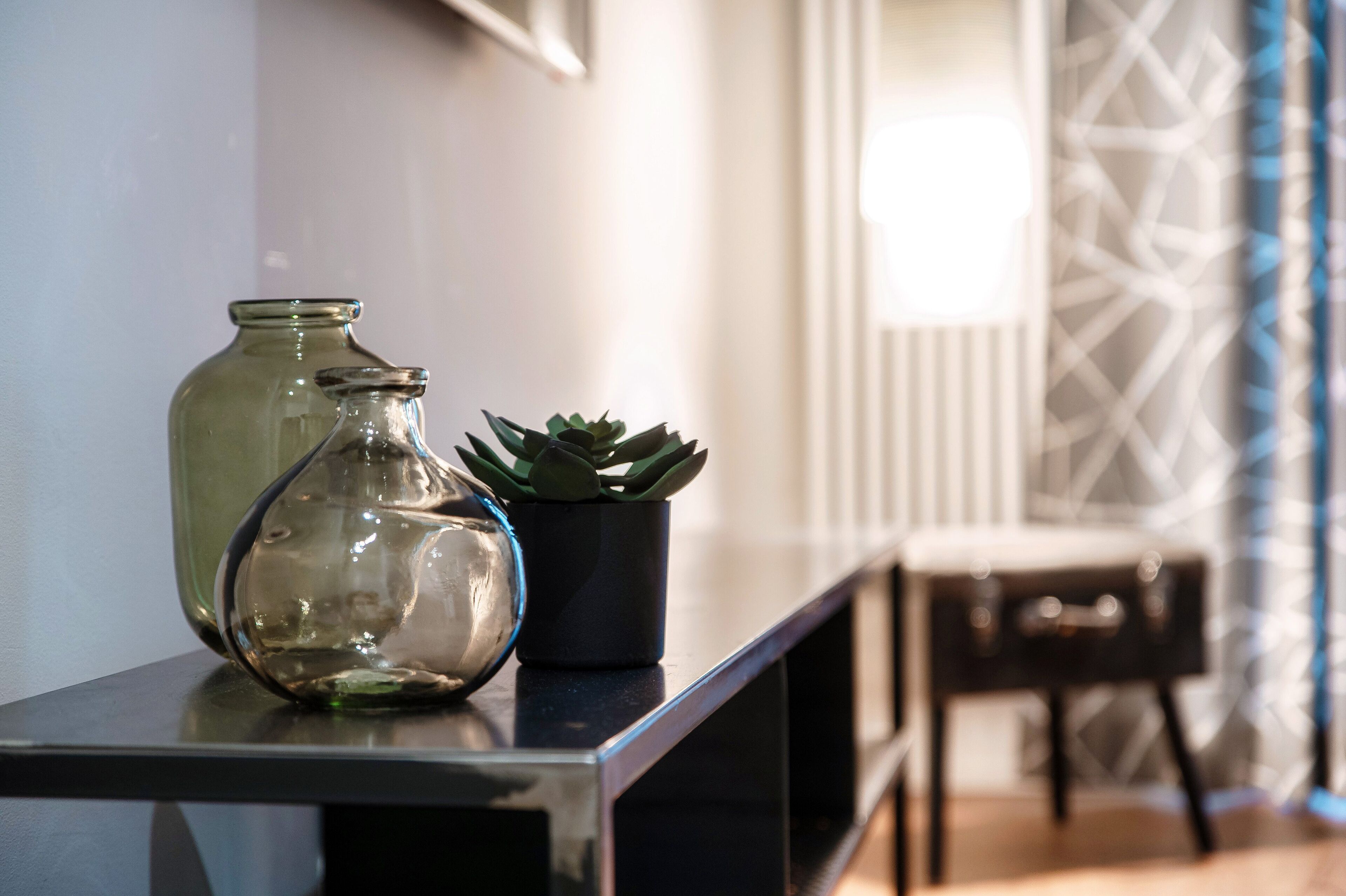 A glass vase and a potted succulent on a black console table.
